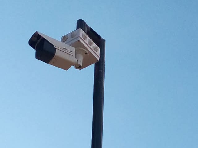 A bullet camera mounted at the top of a steel pole against a clear sky
