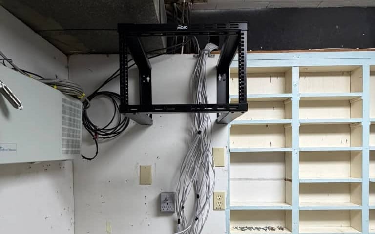 A wall-mounted open network rack with a bundle of grey Ethernet cables being pulled in during an installation